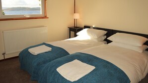 A hotel room with two beds, a window with a view of the sea, a bedside table with a lamp, and a radiator. - Cockleshell Lodge located at the waters edge near Otter Ferry-Pet friendly (Tighnabruaich)