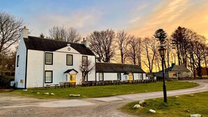 A white building with a black roof, a yellow door, and multiple windows. - Cockleshell Lodge located at the waters edge near Otter Ferry-Pet friendly (Tighnabruaich)
