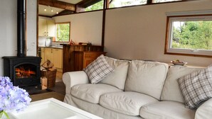 A cozy living room with a beige sofa, a glass coffee table, and a fireplace. - Cockleshell Lodge located at the waters edge near Otter Ferry-Pet friendly (Tighnabruaich)