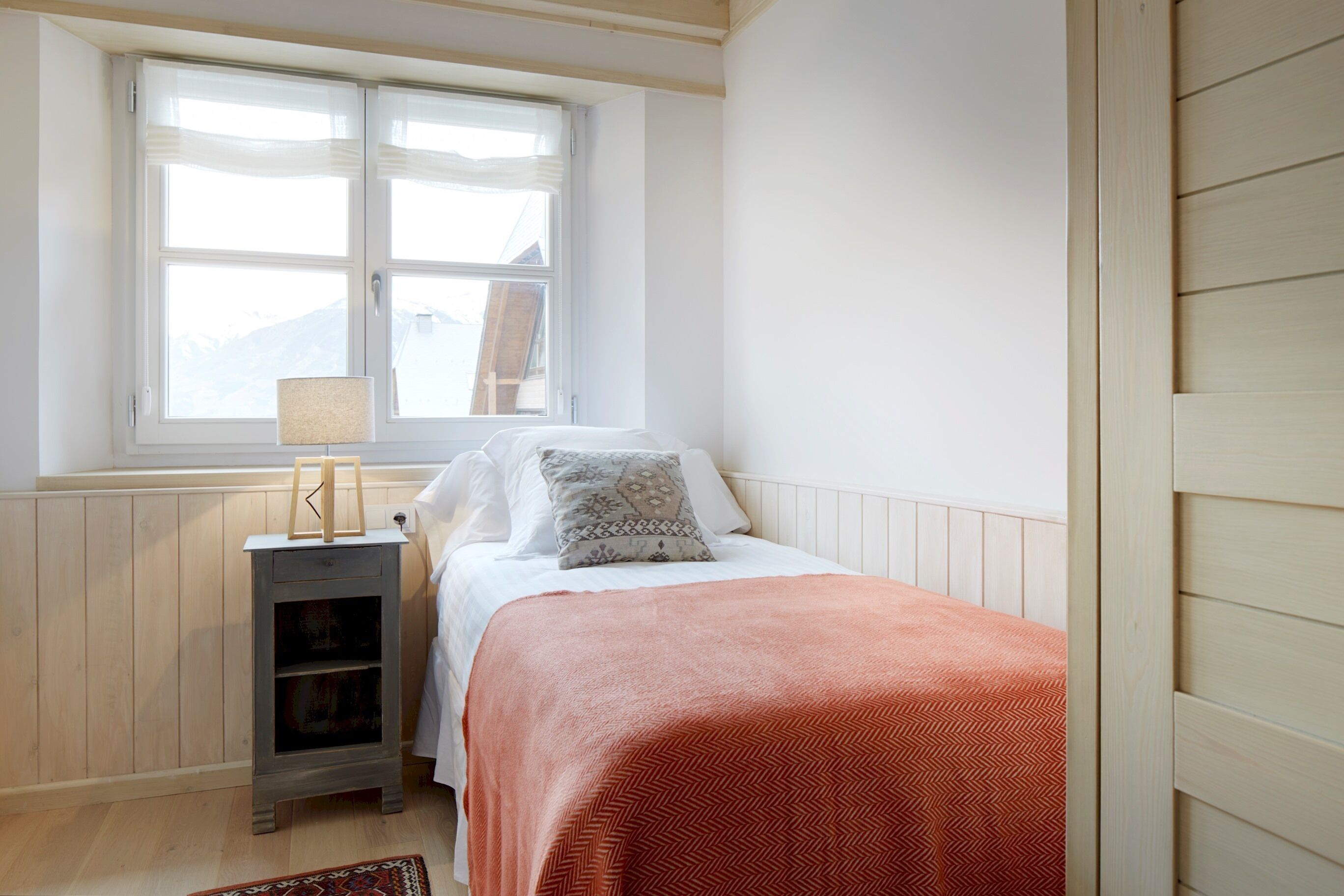 A bedroom with a bed, a nightstand, a window, and a radiator.