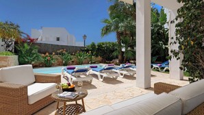 A poolside area with lounge chairs, a wicker sofa, and a table with a book and fruit.