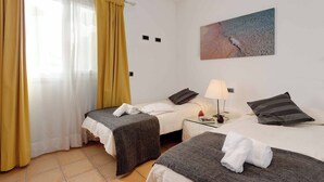 A hotel room with two beds, a painting on the wall, and a window with curtains.