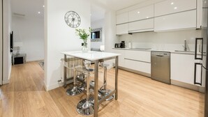 Une cuisine moderne avec des meubles blancs, des appareils en acier inoxydable et une table en verre transparent.