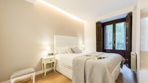 Une chambre à coucher avec un lit, des tables de chevet, un banc et une fenêtre donnant sur un beau paysage.