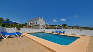 A swimming pool with blue lounge chairs, a white building with stone accents, and a clear blue sky. - Rustic and cheerful holiday home in Javea, Costa Blanca, Spain  with private pool for 6 persons (Javea)