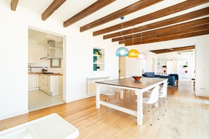 Une cuisine spacieuse avec des meubles blancs, une table à manger en bois et un luminaire suspendu moderne.