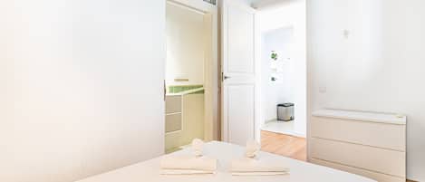 A hotel room with a bed, a wardrobe, a bathroom visible through an open door, and an air conditioning unit on the wall.