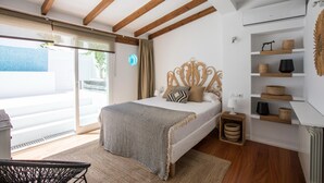 Ein Schlafzimmer mit Bett, Nachttisch, Lampe, einem Regal mit Körben und Blick ins Freie.