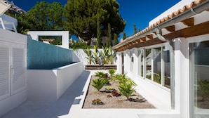 Ein modernes Gebäude mit weißer Fassade, einem Fliesen-Schwimmbecken und einem Gartenbereich mit verschiedenen Pflanzen.
