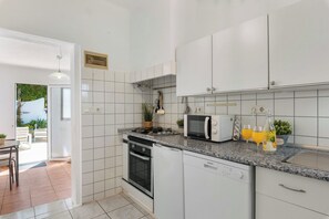 Una cucina moderna con mobili bianchi, forno integrato, microonde e un piano di lavoro in granito.