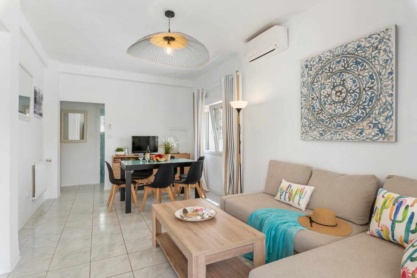 A modern living room with a sofa, a dining table with chairs, a TV, and a ceiling light fixture.