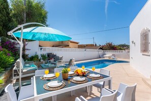 Een eetgedeelte bij het zwembad, met een tafel voor vier personen, een barbecue en een grote parasol voor de schaduw.