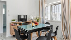 Ett modernt matområde med ett glasbord, svarta stolar, en tv och ett fönster med gardiner.