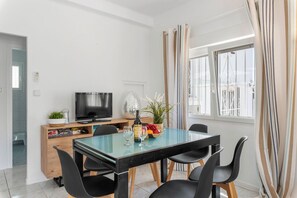 Zona pranzo moderna con tavolo in vetro, sedie nere, televisore e finestra con tende.