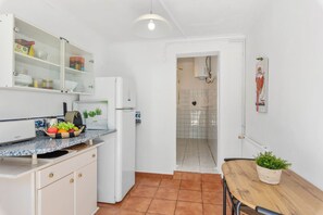 A compact kitchen with a refrigerator, a countertop with a basket of fruit, and a dining area with a table and chair.