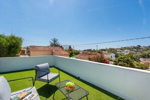 A balcony with artificial grass, a chair, a small table, and a bowl of fruit.