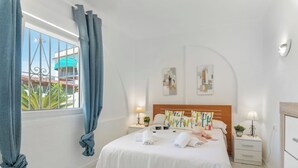 Ett hotellrum med en säng, sängbord, ett fönster med gardiner och konstverk på väggarna.