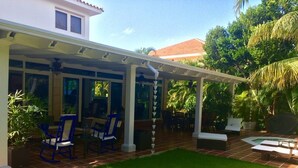 Ein überdachter Patio-Bereich mit Außenbestuhlung, einem Schwimmbad und üppiger Bepflanzung.