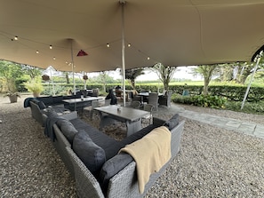 An outdoor patio with a covered seating area, tables, and a grill.