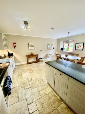 A kitchen with a stove, a sink, a dining table, and chairs. There is a fire extinguisher on the wall and a window with curtains.