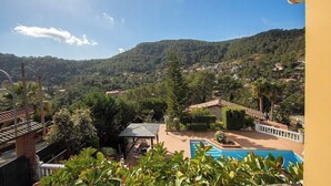 A view of a pool area with a mountain backdrop, surrounded by greenery and a clear sky.