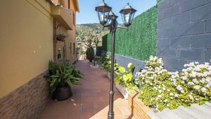 A narrow outdoor corridor with potted plants and a street lamp.
