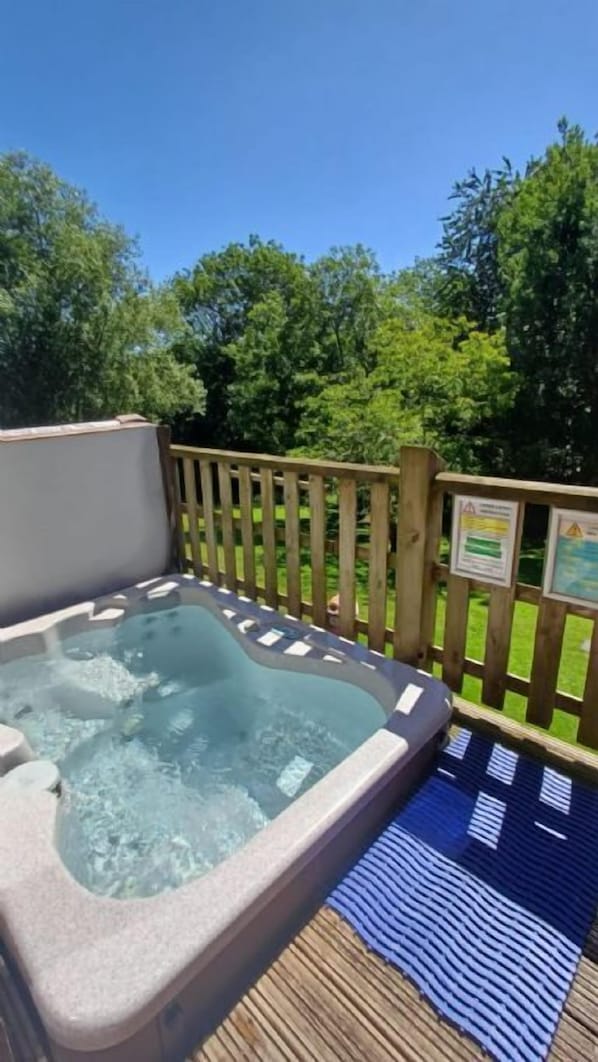 A hot tub on a wooden deck with a blue and white checkered mat, surrounded by a wooden fence and lush greenery.