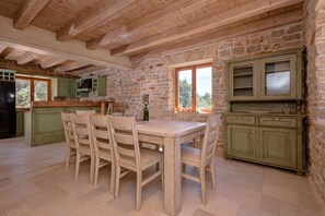 Eine rustikale Küche mit freiliegenden Holzbalken, einer Steinwand und einem Essbereich mit Holzsesseln und einem Tisch.
