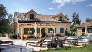 Une villa en pierre avec un toit en tuiles, une piscine et un espace salon extérieur.