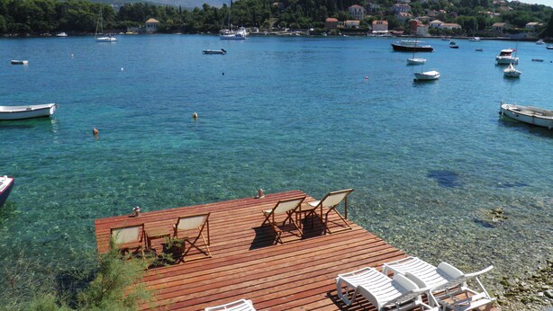 A wooden deck with clear blue water, boats, and a distant town.