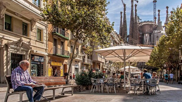 An outdoor café area with tables and chairs, benches, and a person sitting on a bench.