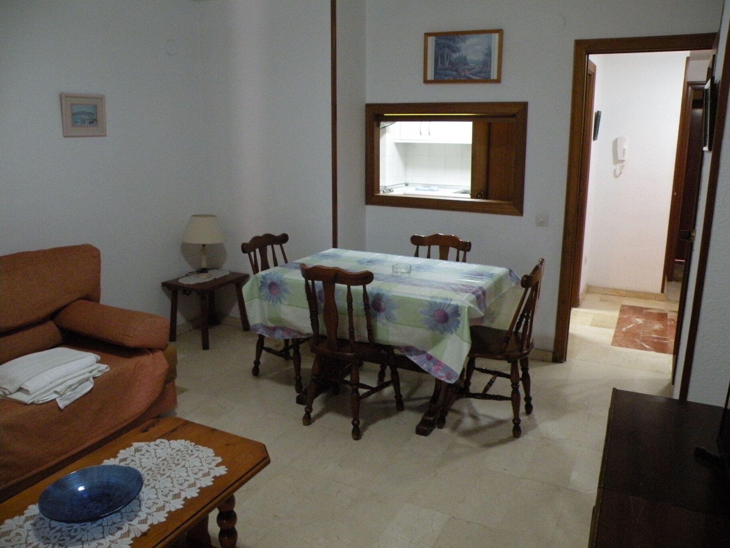 A dining area with a table set for four, surrounded by wooden chairs. A small table with a bowl and a lace tablecloth is in the foreground.
