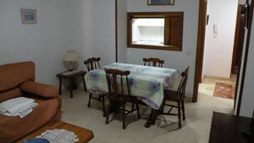 A dining area with a table set for four, surrounded by wooden chairs. A small table with a bowl and a lace tablecloth is in the foreground.