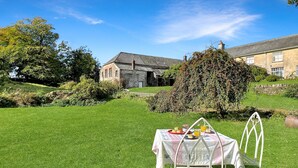 A grassy lawn with a table set for breakfast, a stone building, and a large tree in the background.