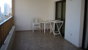 A balcony with a white plastic chair, a small white table, and a window with curtains. - FINLANDIA (1 BEDROOM) (Benidorm)