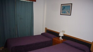 A room with two beds, a nightstand with a lamp, a painting on the wall, and a blue curtain. - FINLANDIA (1 BEDROOM) (Benidorm)