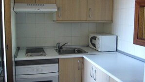 A compact kitchen with wooden cabinets, a built-in oven, a microwave, and a sink. - FINLANDIA (1 BEDROOM) (Benidorm)