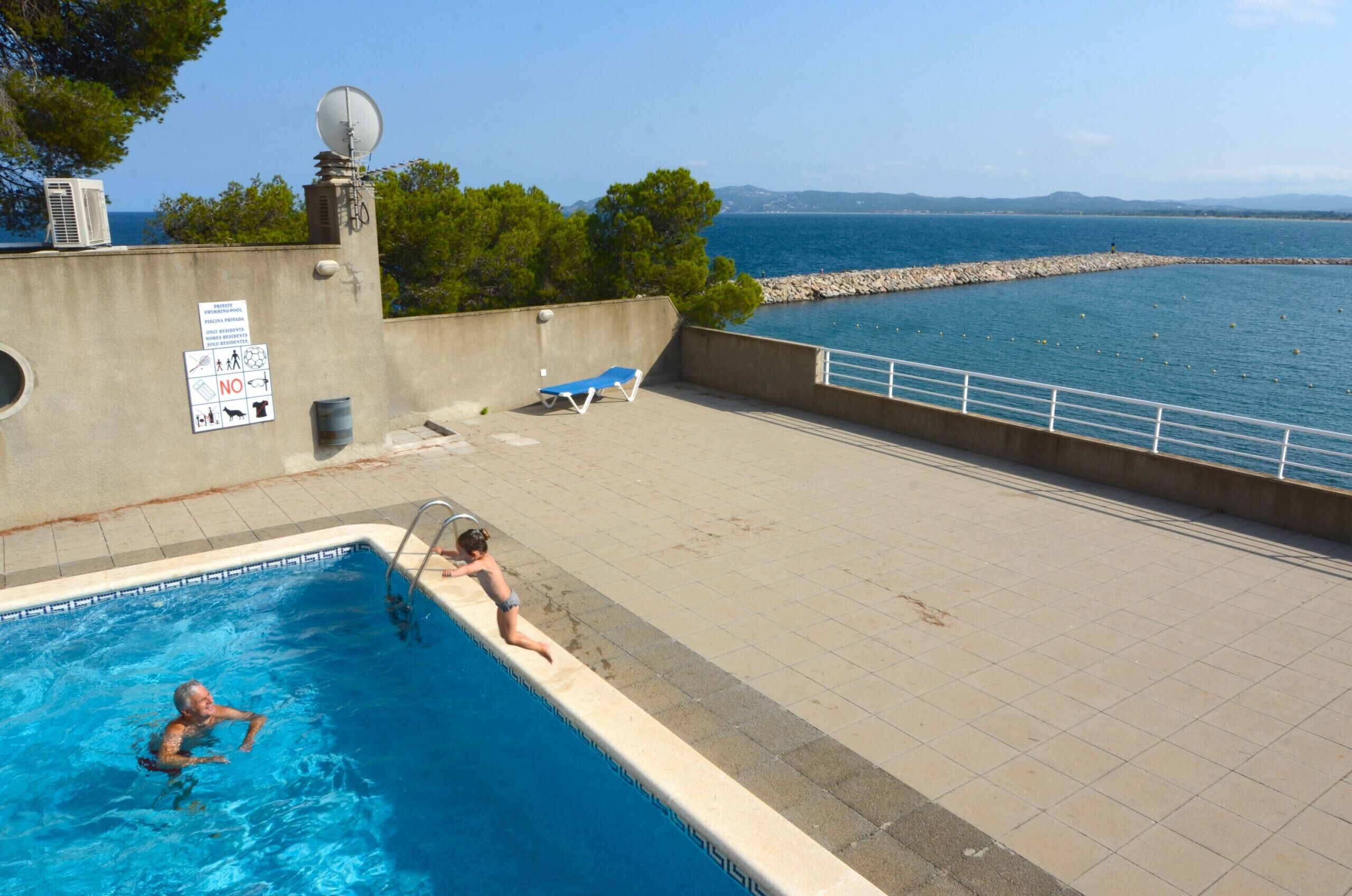 Une piscine avec vue sur la mer, un poste de surveillance pour les sauveteurs et un panneau indiquant les consignes de sécurité.