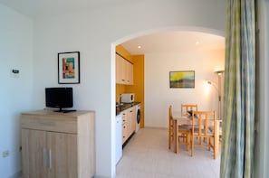 Un espace de vie compact comprenant un coin cuisine, un coin repas et un téléviseur posé sur un meuble en bois.