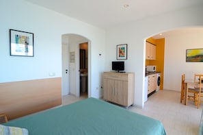 Une chambre comprenant un lit, une armoire en bois avec un téléviseur, un petit coin cuisine et un espace repas.
