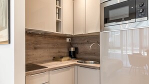 A modern kitchen with white cabinets, a wooden backsplash, a stainless steel sink, and a built-in microwave. - Luxury Apartment Marigold in Split (Split)