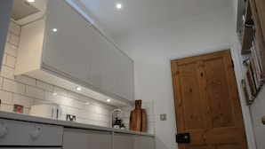 A kitchen with white cabinets, a wooden door, and a tiled backsplash. - 'The Snug' nr York: stunning self-contained studio @ Old Station Master's House. (Riccall)