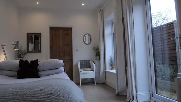 A bedroom with a bed, a chair, a door, a window, and a mirror. - 'The Snug' nr York: stunning self-contained studio @ Old Station Master's House. (Riccall)