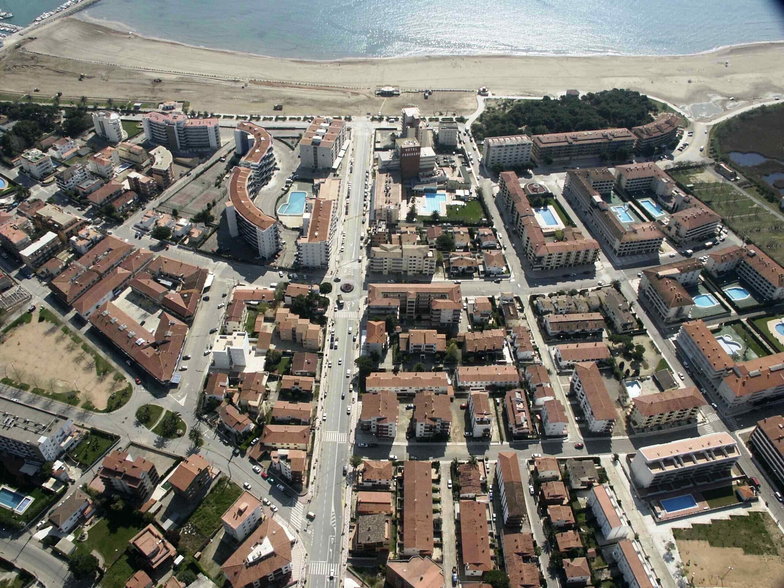 Vista aérea de una ciudad costera con una combinación de edificios residenciales y comerciales, una avenida central y una playa al fondo.