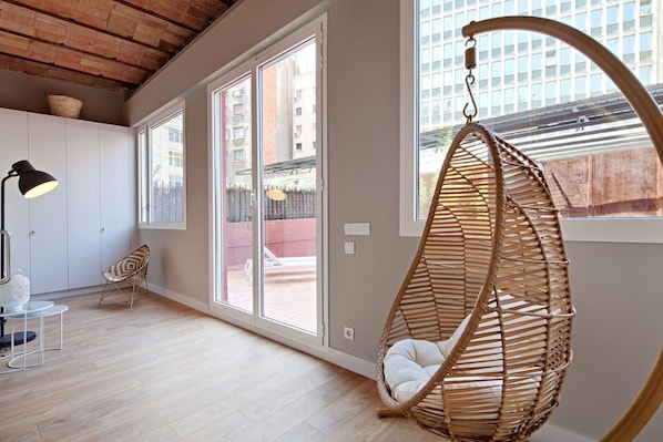 A room with a hanging chair, a lamp, a chair, and a view of the outside. - Barcelona Plaza Catalunya Flat with Huge Terrace (Barcelona)