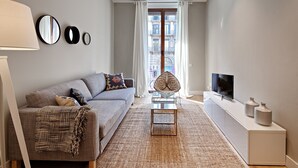 Un salon moderne avec un canapé, une table basse, un téléviseur et une vue sur la ville grâce à de grandes fenêtres.