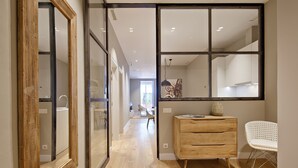 Un couloir avec une commode en bois, une chaise blanche et un grand miroir.