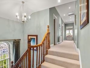 Un escalier avec des balustrades en bois et des marches recouvertes d’une moquette beige, menant à un palier.