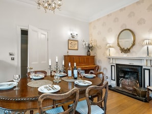 Une salle à manger avec une table en bois dressée pour quatre personnes, une cheminée et un lustre.