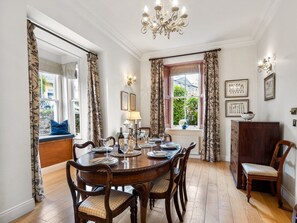 A dining room with a round table set for six, surrounded by wooden chairs.